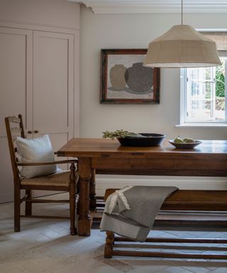 kitchen diner with wooden trestle table, wooden bench and chair, linen pendant and pale pink cabinet