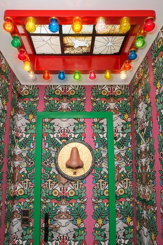 A doorway with a nose decoration on it, patterned wallpaper and a multi coloured lights above it.
