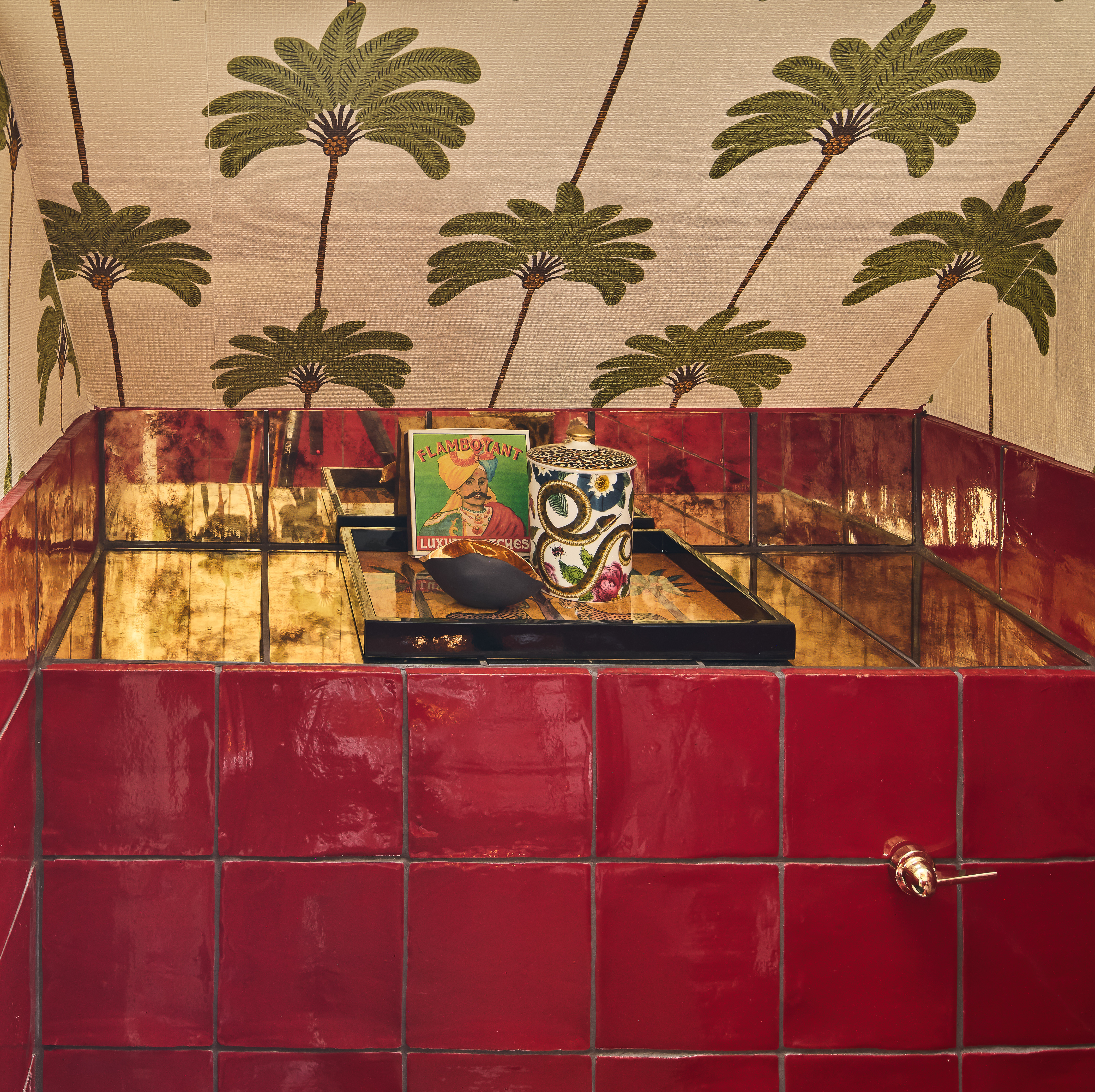 A red tiled bathroom with palm wallpaper and gold details