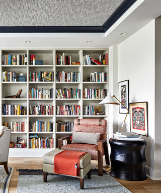 A room with one wall lined with full bookshelves, and an armchair in front.