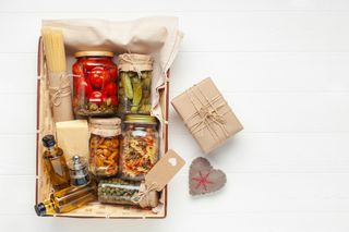 A food hamper containing various foods in jars such as gherkins, olives, pasta, and oils.