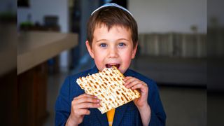 Young boy wearing a yarmulke taking a bit out of unleavened bread