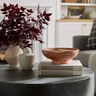 A coffee table with two books, a marble orange bowl, and a vase with a purple floral arrangement