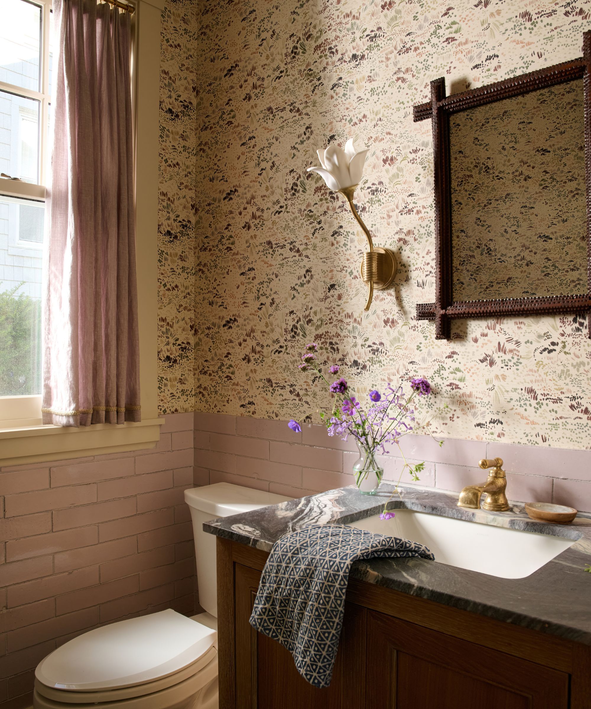 A powder room with mauve tiles on the lower walls and a small-scale floral wallpaper above.