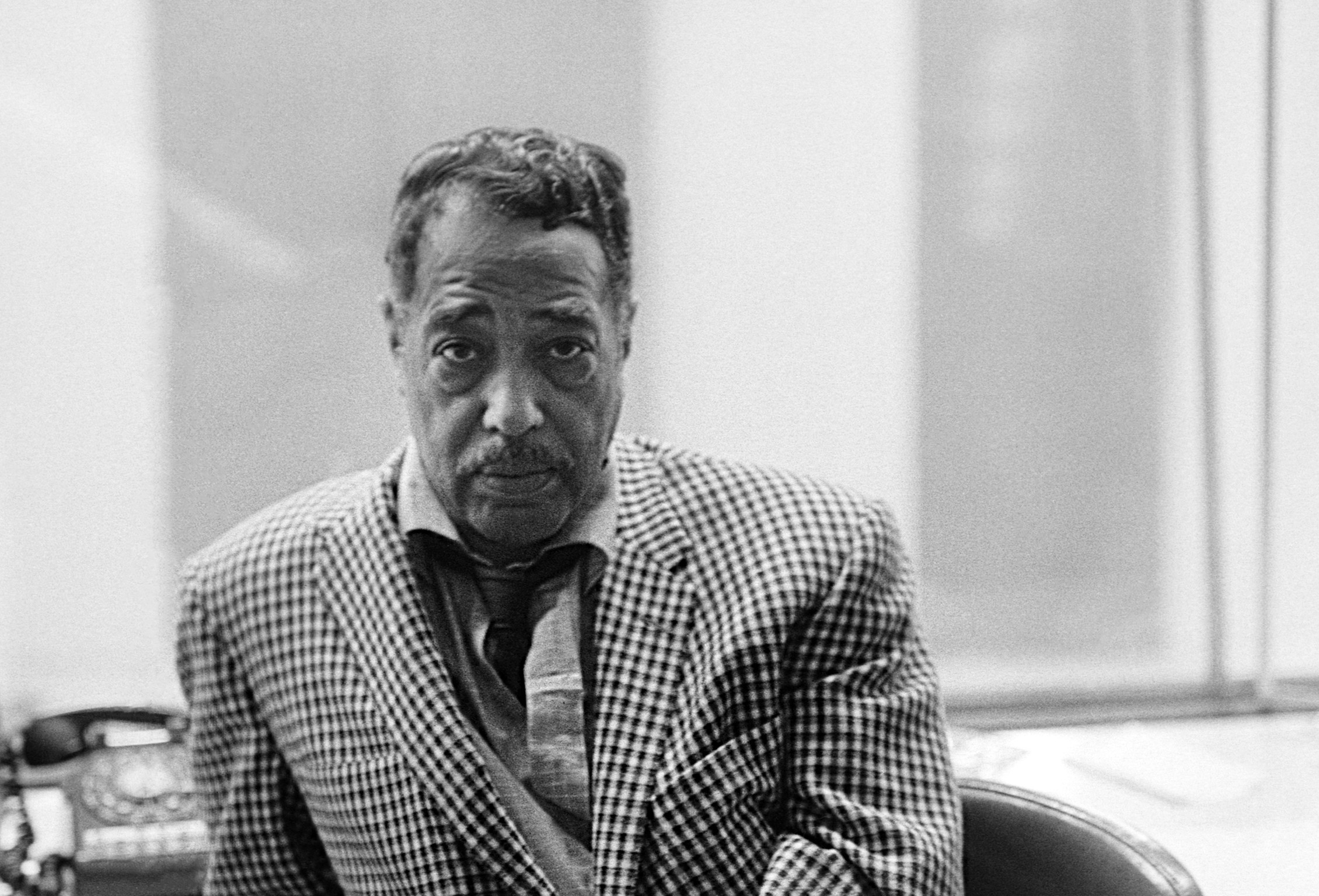A black and white, close-up portrait of Duke Ellington wearing a checkered blazer and looking directly at the camera.