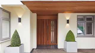 contemporary porch with wooden slatted overhang, slate tiles on floor, dark oak door and screen and black down and uplighters on cream rendered house exterior walls