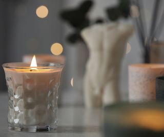 A lit candle on a countertop with a figurine in the background