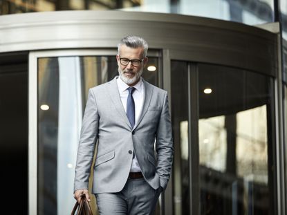 Mature businessman leaving office building. Confident male professionals is walking outside workplace after work. He is wearing suit.