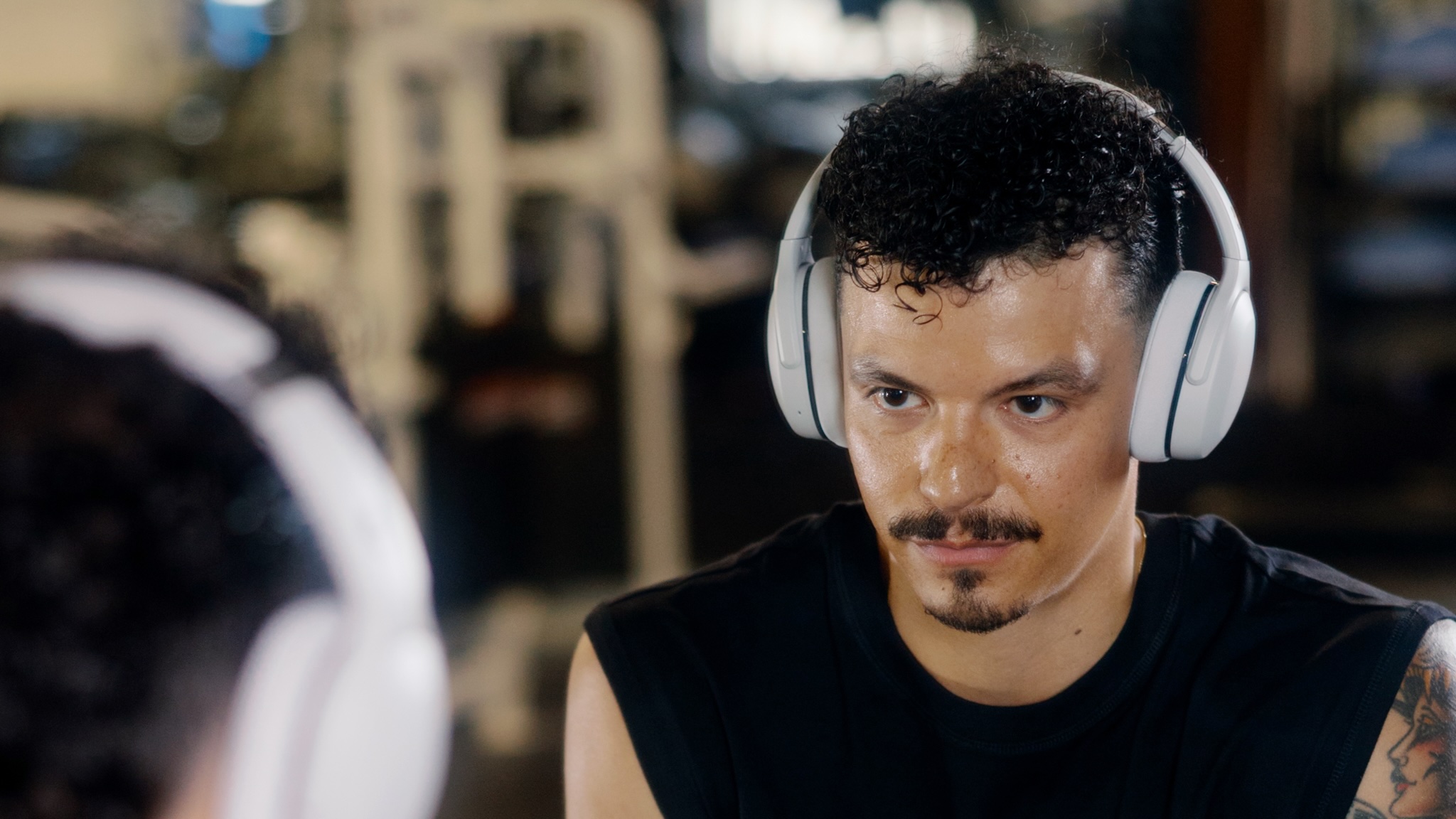 A man wearing Skullcandy Crusher 540 Active headphones looking at himself in the gym mirror