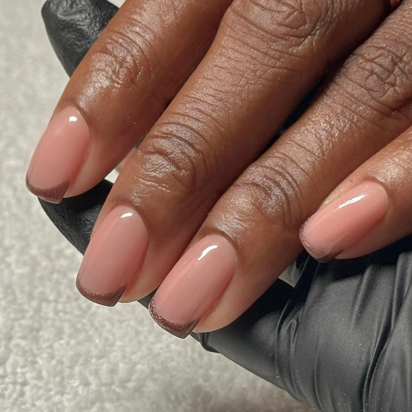 A short, square, brown, cat-eye French tip manicure