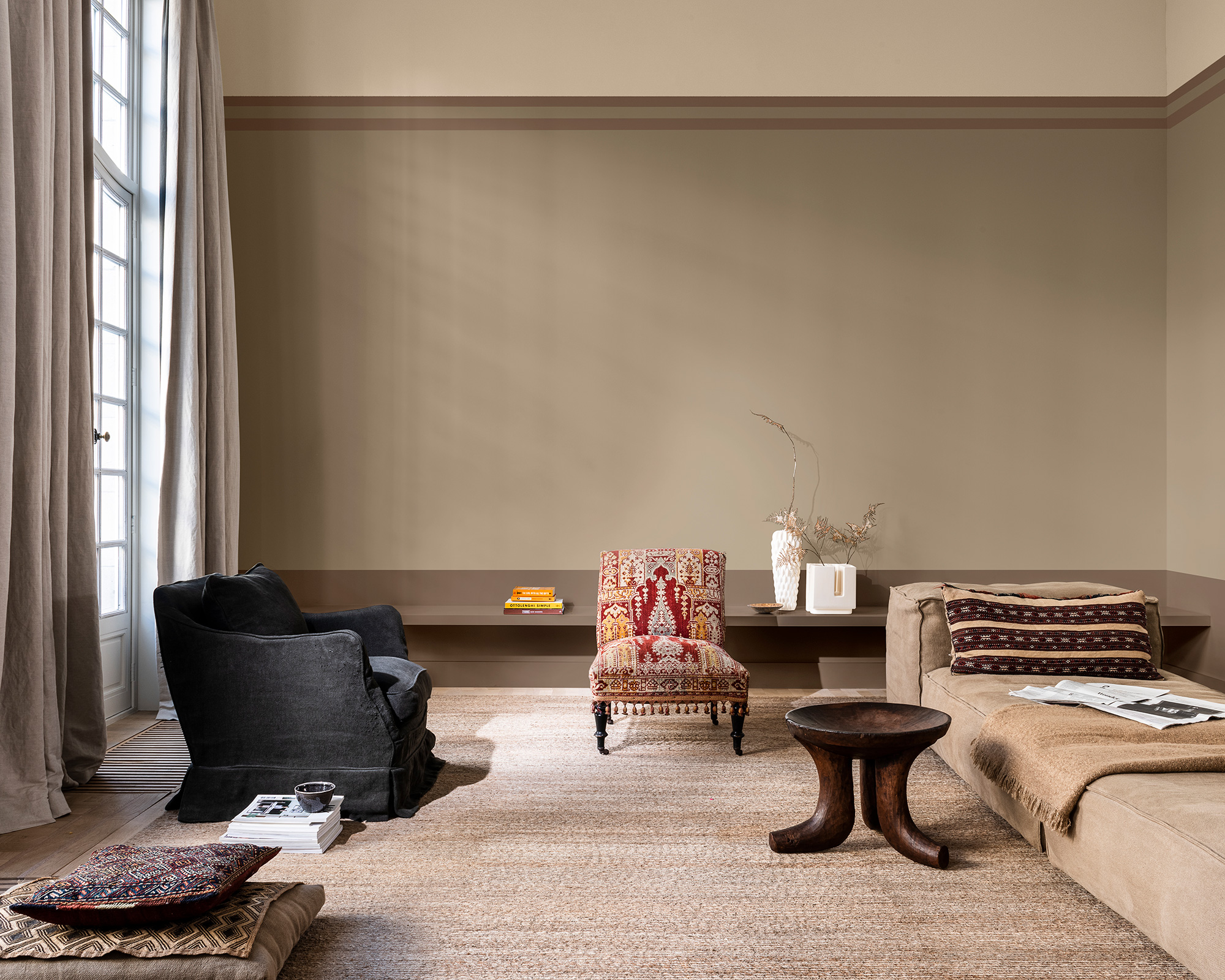 Living room color schemes shown here in a layered beige scheme with brown accents and a patterned red vintage armchair.