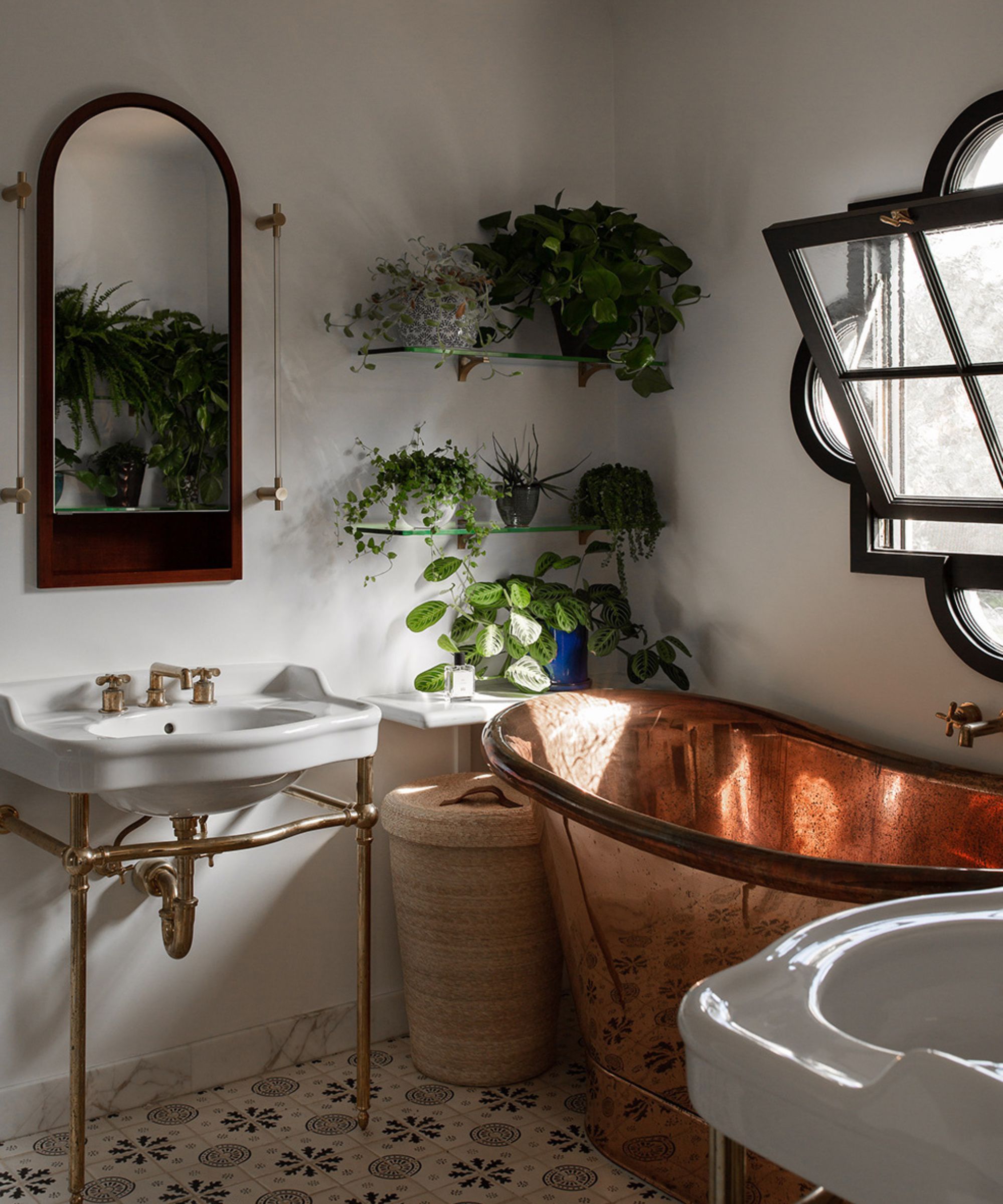 A Mediterranean bathroom with patterned floor tiles, a copper bathtub, an arched vanity mirror, and a unique window