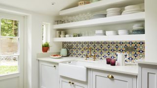 Harvey Jones white shaker kitchen with colorful splashback tiles, open shelves and a butler sink with gold taps