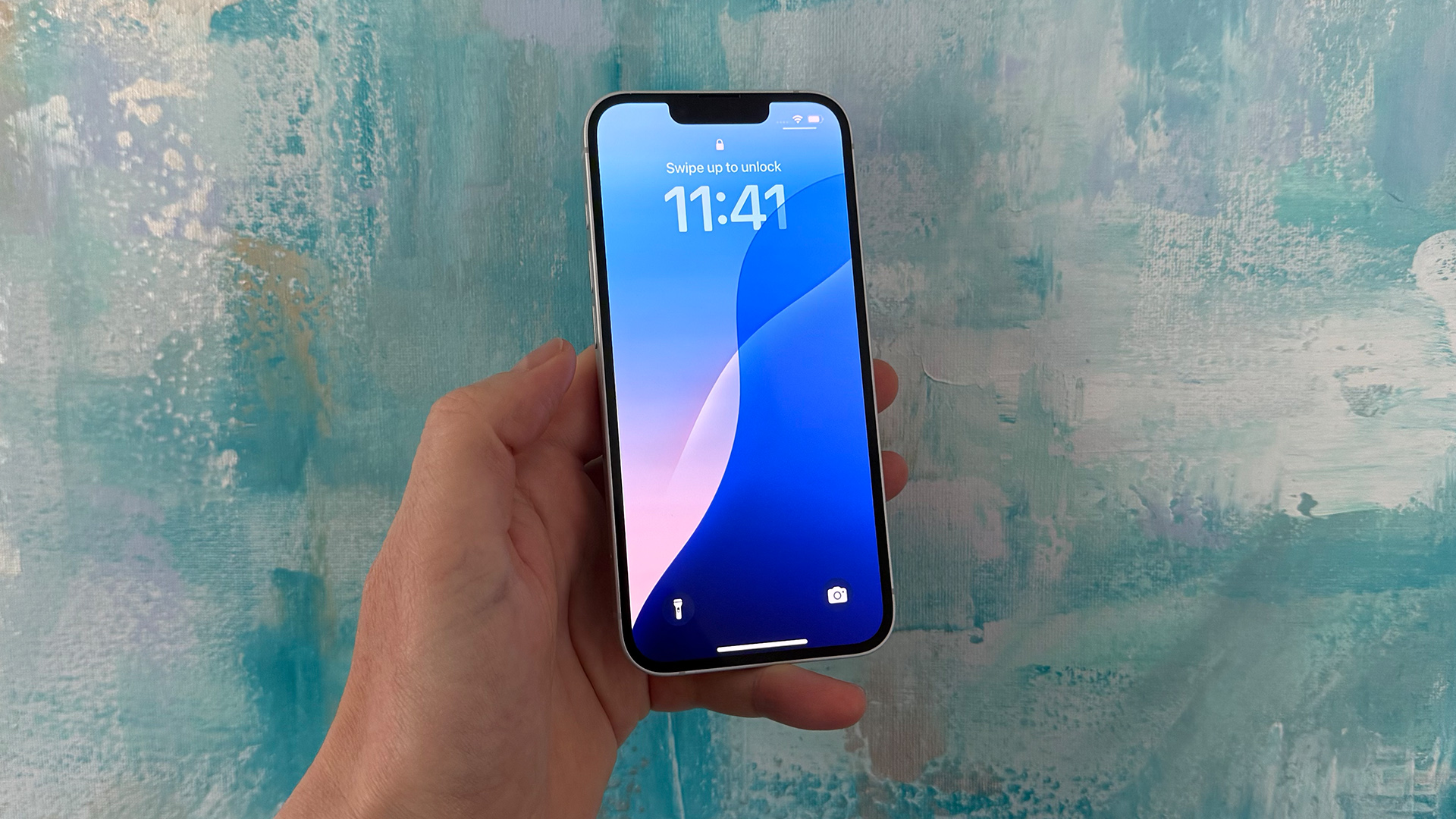 Apple iPhone 16e smartphone held in hand in front of canvas painting, showing time on screen