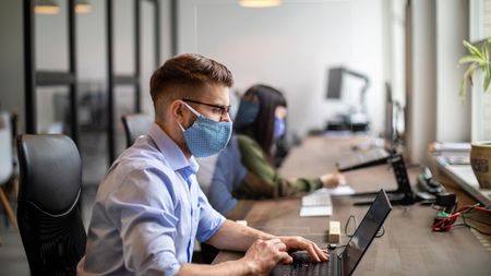 Business people back to work after pandemic sitting at desk with protection guard between them