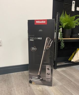 Miele Triflex HX2 Pro original packaging on laminate floor in front of shelves and plants in Future test center