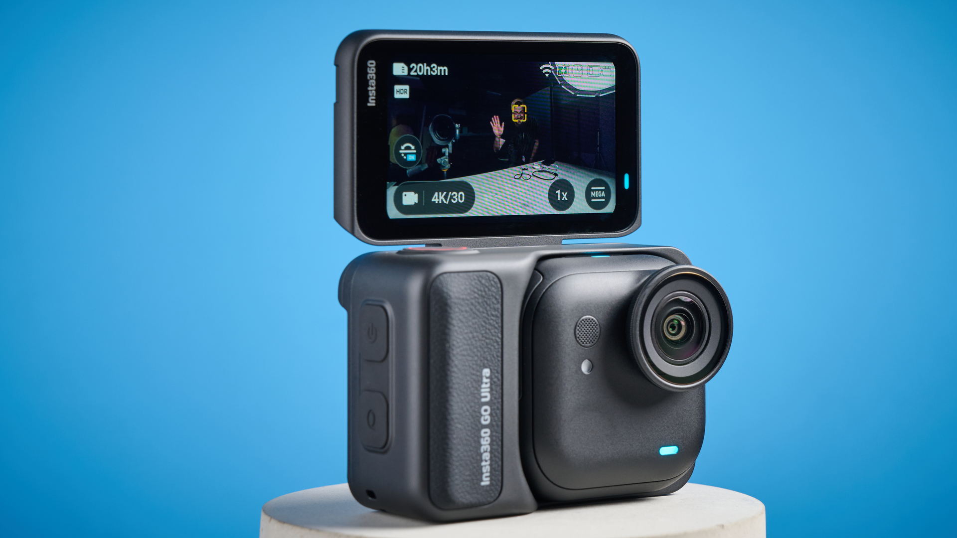 Insta360 Go Ultra with its selfie screen flipped up and a man waving in the image, with face detection tracking his face, all against a blue background