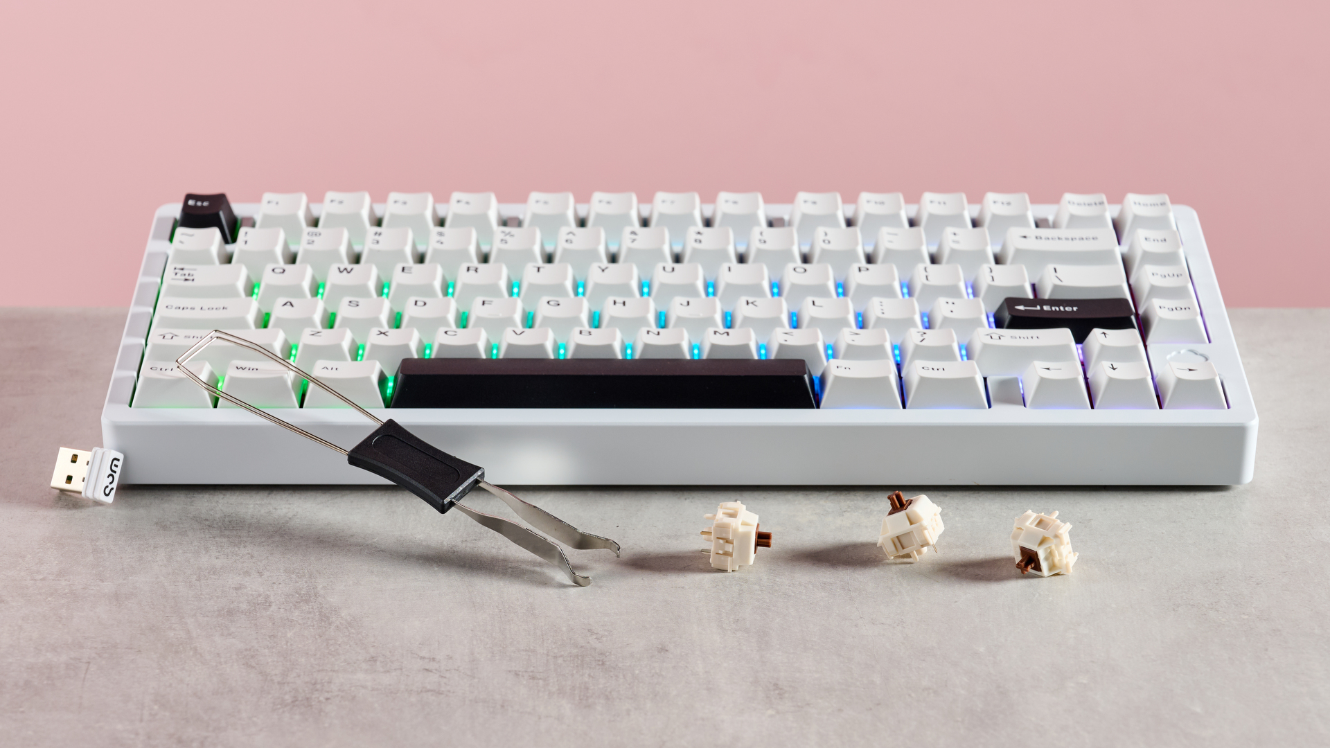Wobkey Rainy 75 Pro with keycap puller, USB 2.4GHz dongle, and three spare switches on desk with pink background