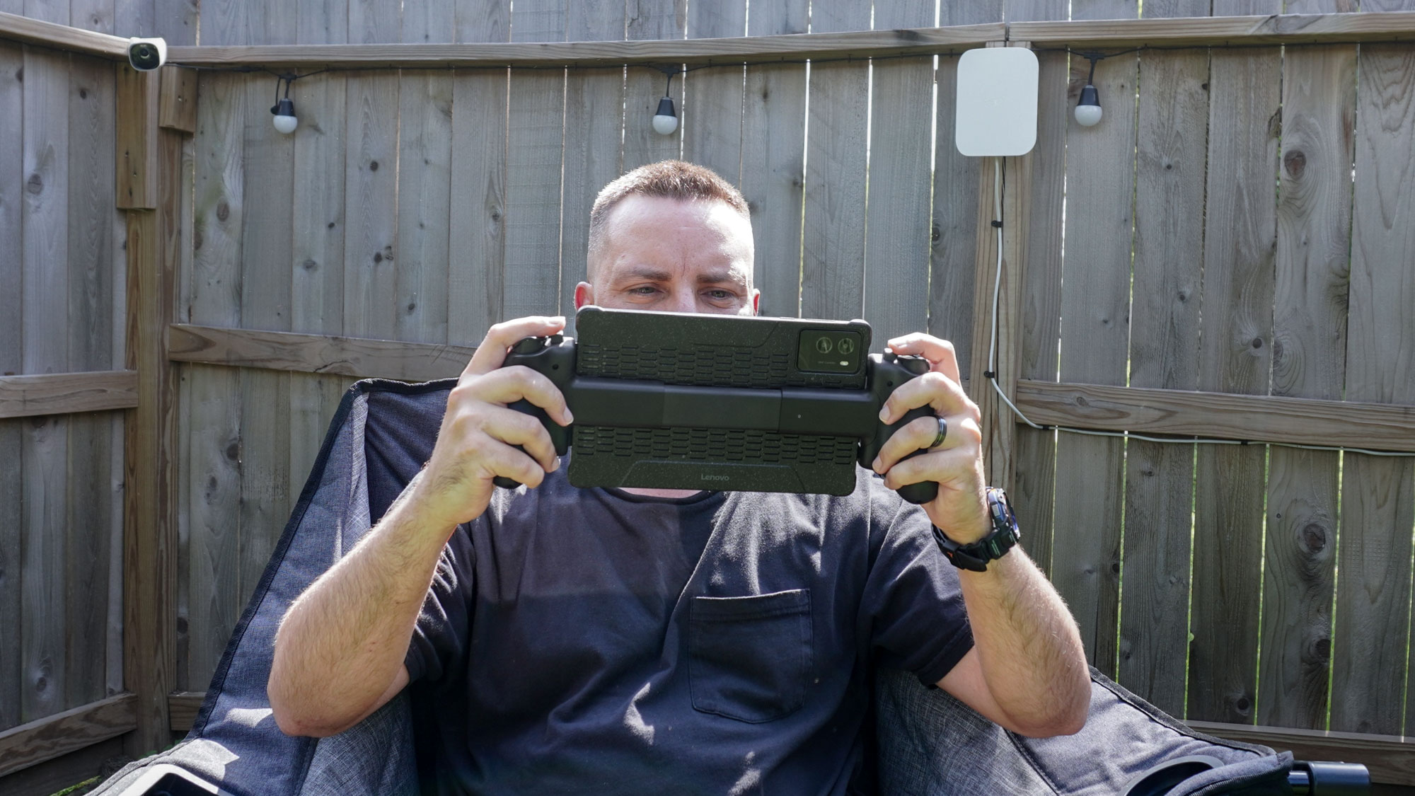 Playing games remotely on a tablet with the Razer Kishi Ultra mobile game controller while sitting in The Foldable Gaming Chair out in the backyard with the eero Outdoor 7 mesh extender in the background
