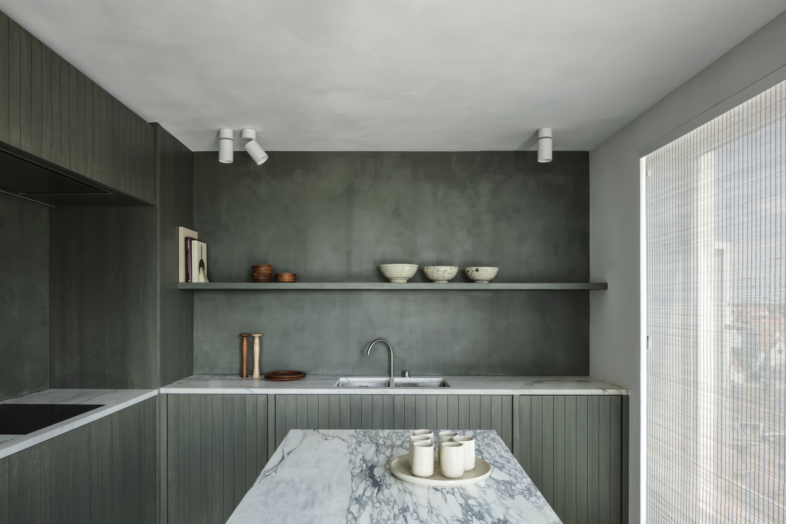 A kitchen finished in limewash paint in olive green color, with the island in veined marble