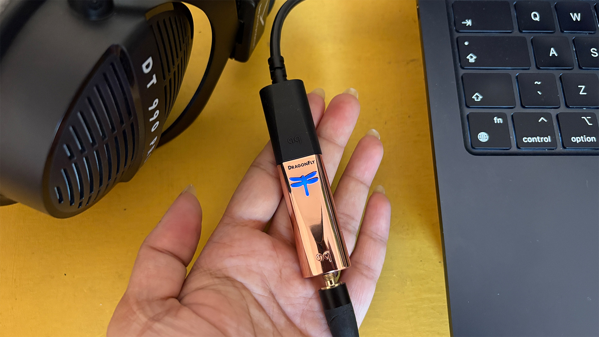 AudioQuest DragonFly Copper DAC held in hand between headphones and laptop