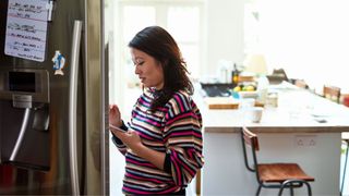 Woman opening fridge and looking at phone