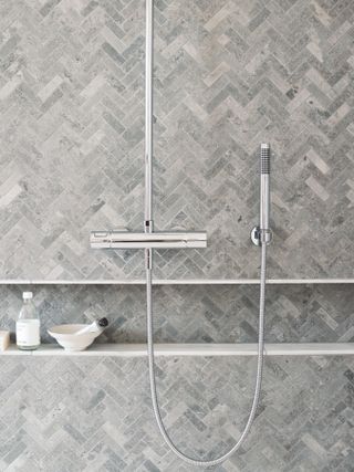 grey toned herringbone subway tiles in shower with recessed shelf unit
