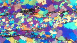 A microscopic view of a thin piece of polished rock from Jack hills. A gypsum plate on the microscope allowed scientists to see a rainbow spectrum of quartz. Rocks from Jack Hills are 99% quartz, and the remaining 1% includes precious zircons.
