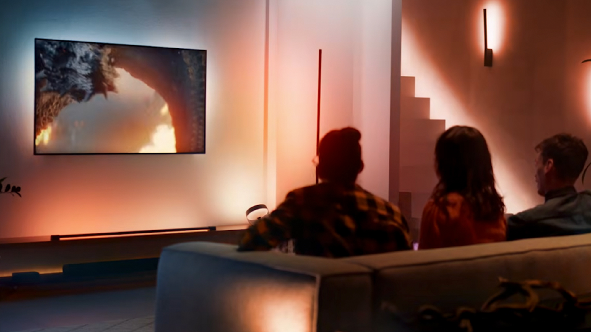 A view from the back corner of a room of three people watching tv with a Philips Hue setup