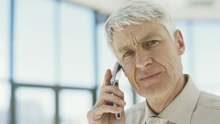 An older man looks questioning while holding a flip phone to his ear.
