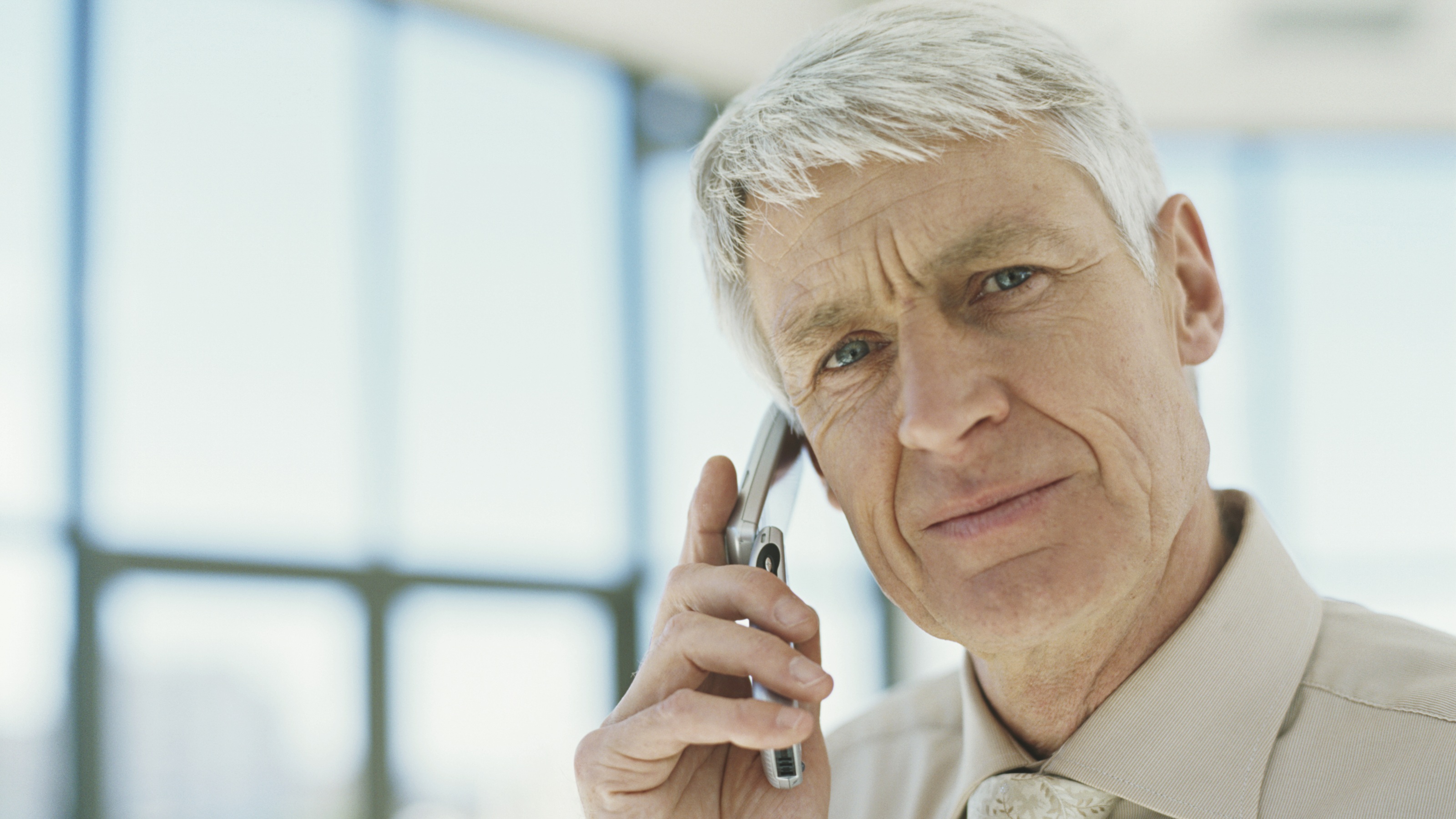 An older man looks questioning while holding a flip phone to his ear.