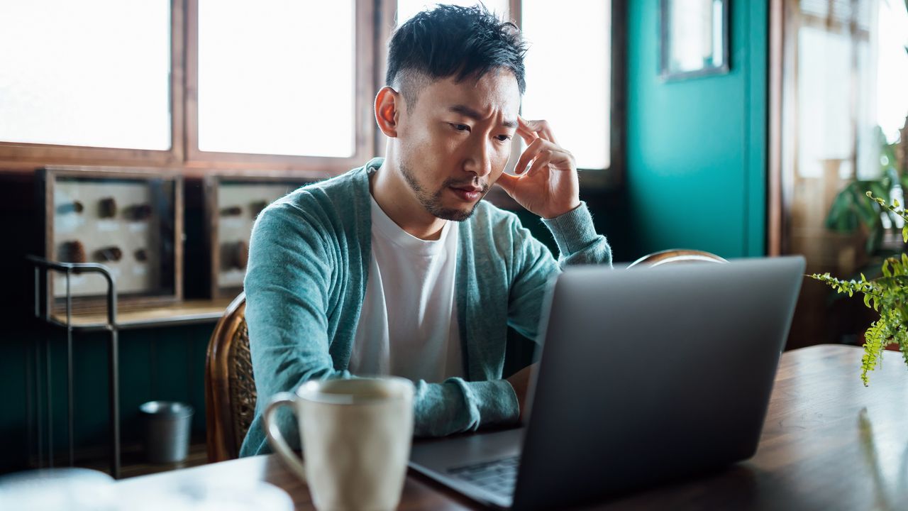 A young man looks unhappy as he sits at his desk in an office and looks at her computer.