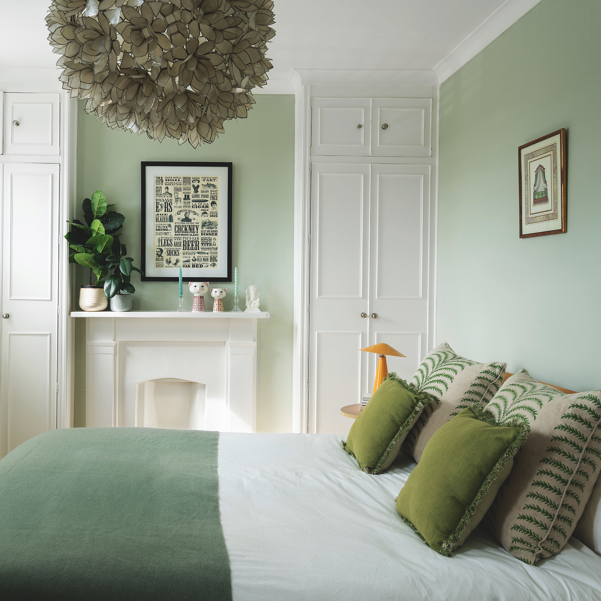bedroom with pale sage green painted walls, white fireplace and white storage wardrobes built into alcoves