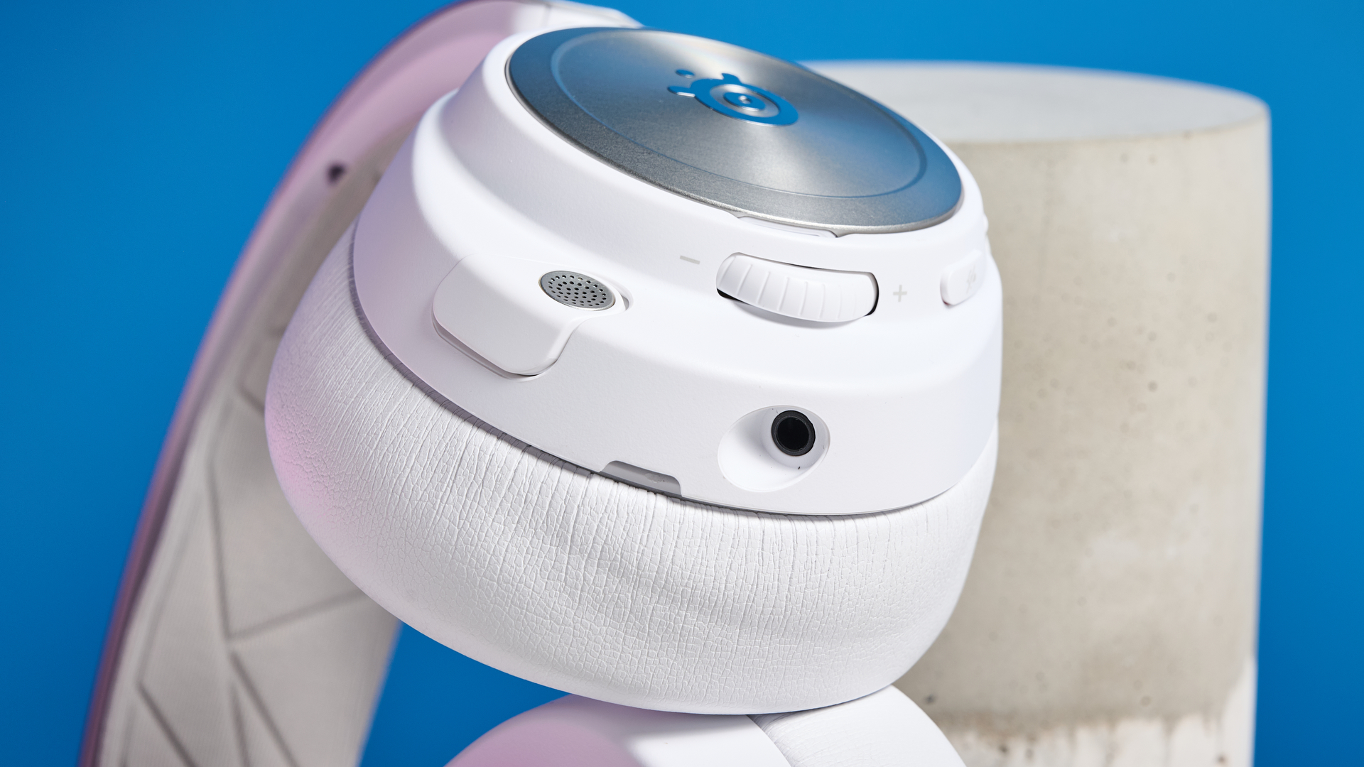 SteelSeries Arctis Nova Pro Wireless in white on a stone surface with a gentle purple reflection on the headset