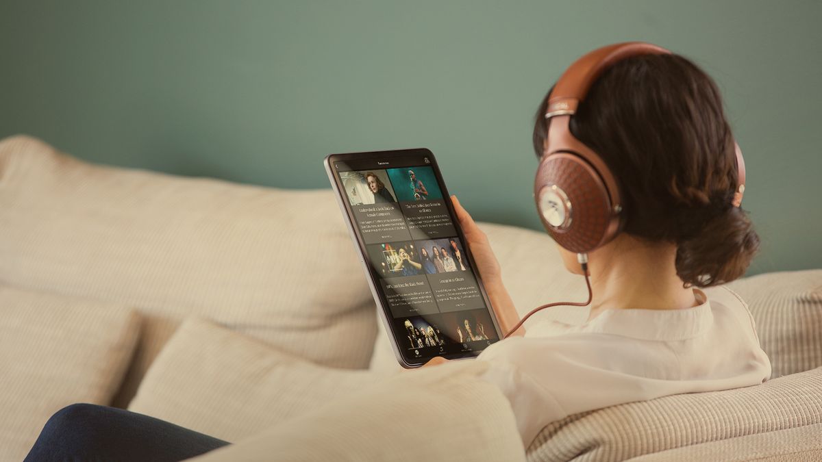 A woman holding a tablet, streaming Qobuz music with Focal Stellia over-ear headphones