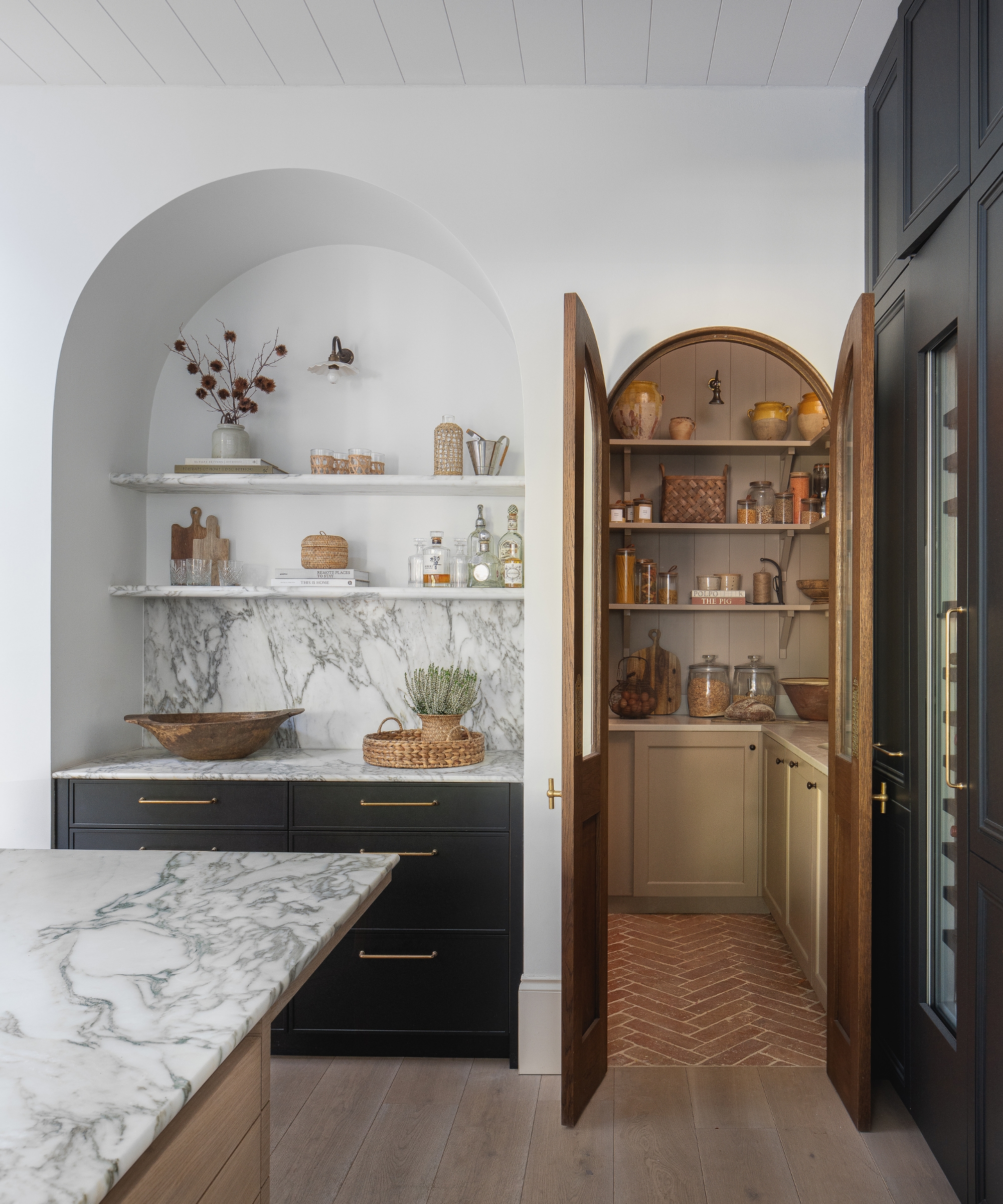 The corner of a kitchen with an arched bar area and a wood arched door into the pantry