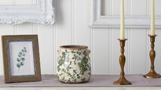 A wooden photo frame, a decorative vase, and dinner candles on a side table from QVC. 
