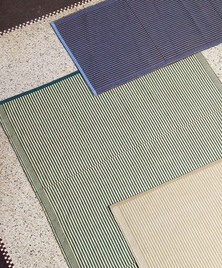 Striped rugs in green, beige and blue placed over each other