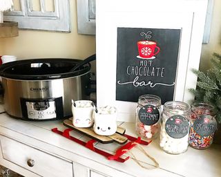 A hot chocolate bar in kitchen with slow cooker containing beverage and mason jars containing an assortment of toppings