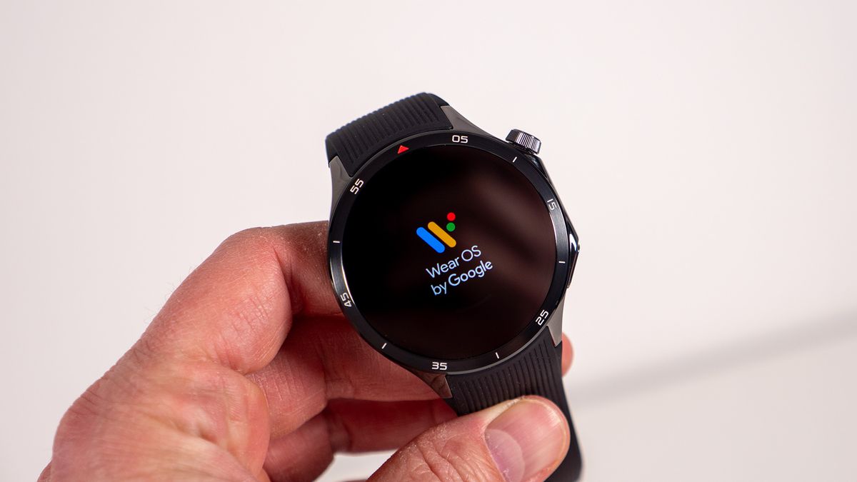 Holding a black OnePlus Watch 3 with the Wear OS logo on its display