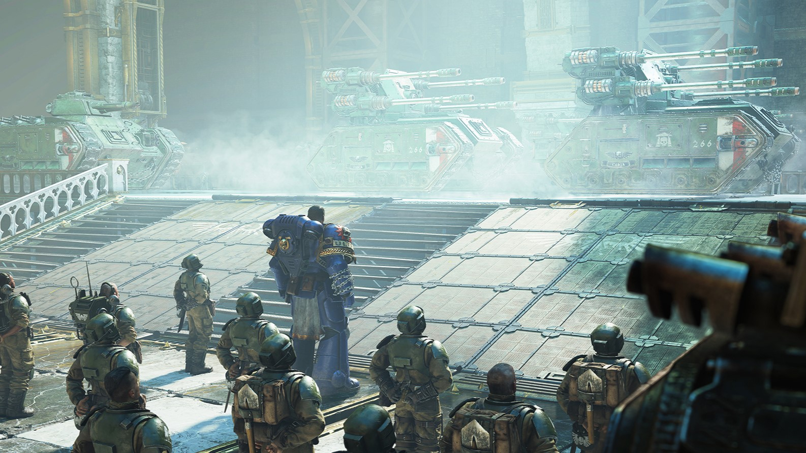 Screenshot from Warhammer 40,000 Space Marine 2 showing an Ultramarine and guardsmen inspecting tanks