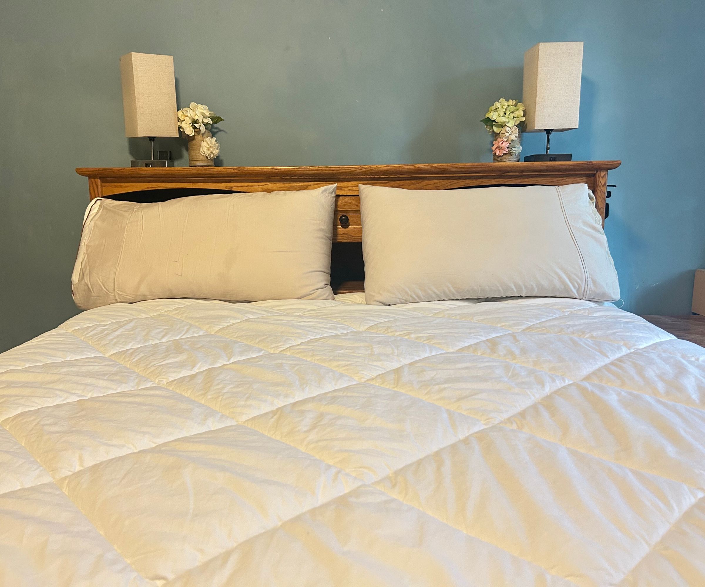 Saatva down alternative comforter on a bed with pillows and a wooden shelf with lamps on behind