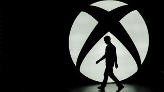 The silhouette of Ralph Fulton, design director for Forza Horizon at Playground Games, is seen walking past the Microsoft Corp. Xbox One logo uring a media event ahead of the E3 Electronic Entertainment Expo in Los Angeles, California, U.S., on Monday, June 9, 2014. Microsoft Corp. and Sony Corp. are gearing up for the next phase of competition between their dueling video-game consoles, highlighting exclusive titles that will be on sale for the year-end holiday season. Photographer: Patrick T. Fallon/Bloomberg via Getty Images 