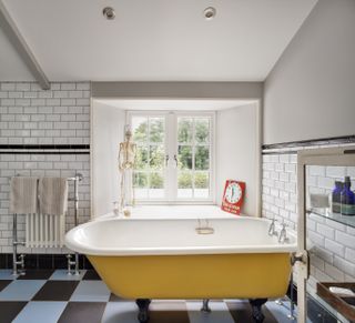 Yellow freestanding bathtub in white bathroom with blue and black tiled floor