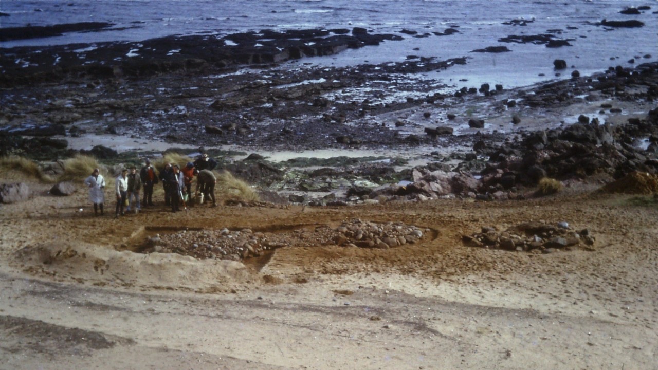 Photograph of the 1965 Lundin Links excavation showing burials. Overhead shot of team standing on a beach.