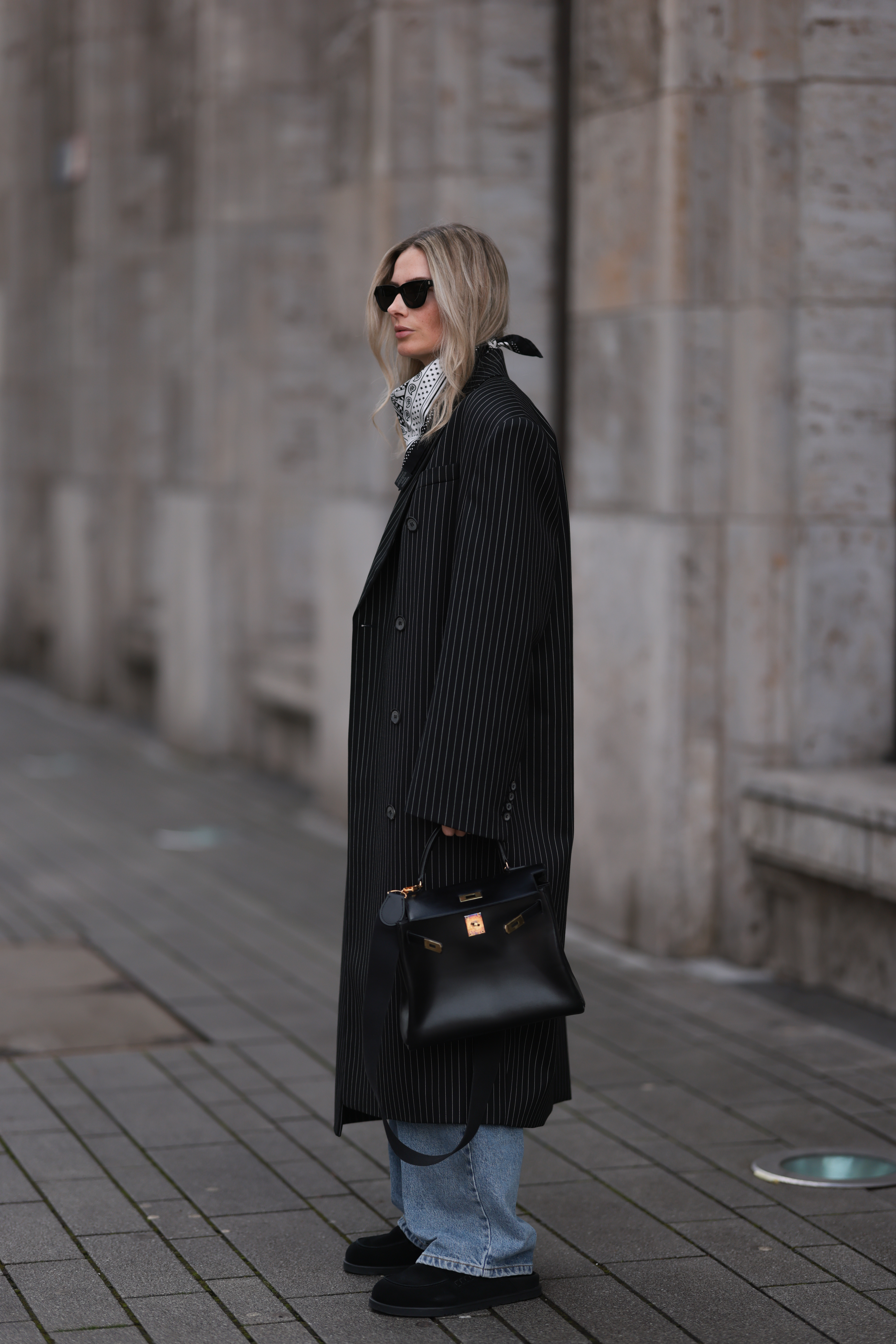 DUSSELDORF, GERMANY - MARCH 19: Kathrin Bommann seen wearing Saint Laurent black sunglasses, Herm&amp;egrave;s black and white bandana, Magda Butrym pinstripes black grey long coat, Raey wide leg blue denim jeans, Skims white top, Herm&amp;egrave;s vintage Kelly black leather bag, Herm&amp;egrave;s black leather loafer, on March 19, 2023 in Dusseldorf, Germany. (Photo by Jeremy Moeller/Getty Images)