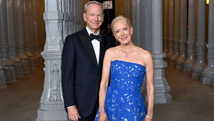 A man wearing a black suit and bowtie stands to the left of a woman in a sparkly blue dres. 