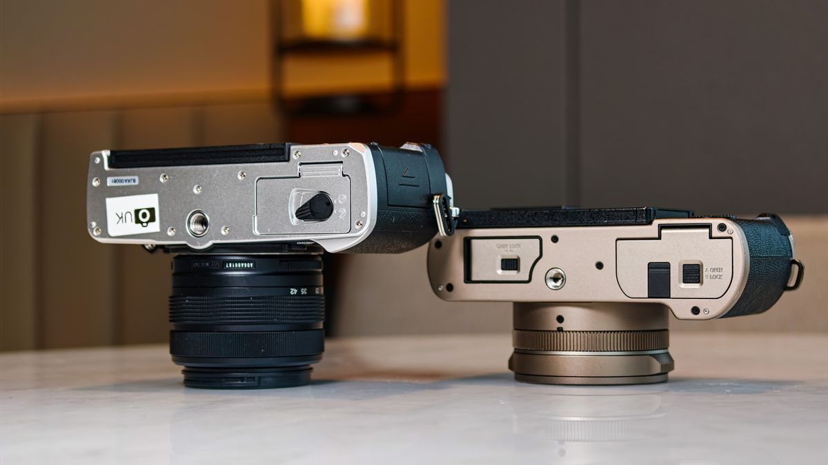 OM System PEN vs Panasonic Lumix L10: two micro four thirds cameras side by side on a white marble surface with lamp light in the background