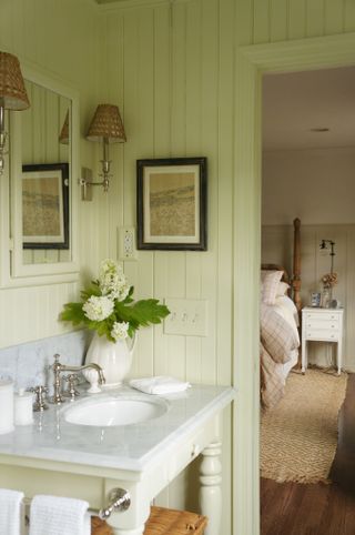 Cream bathroom with vanity, white flowers and frames on the wall looking onto the master bedroom