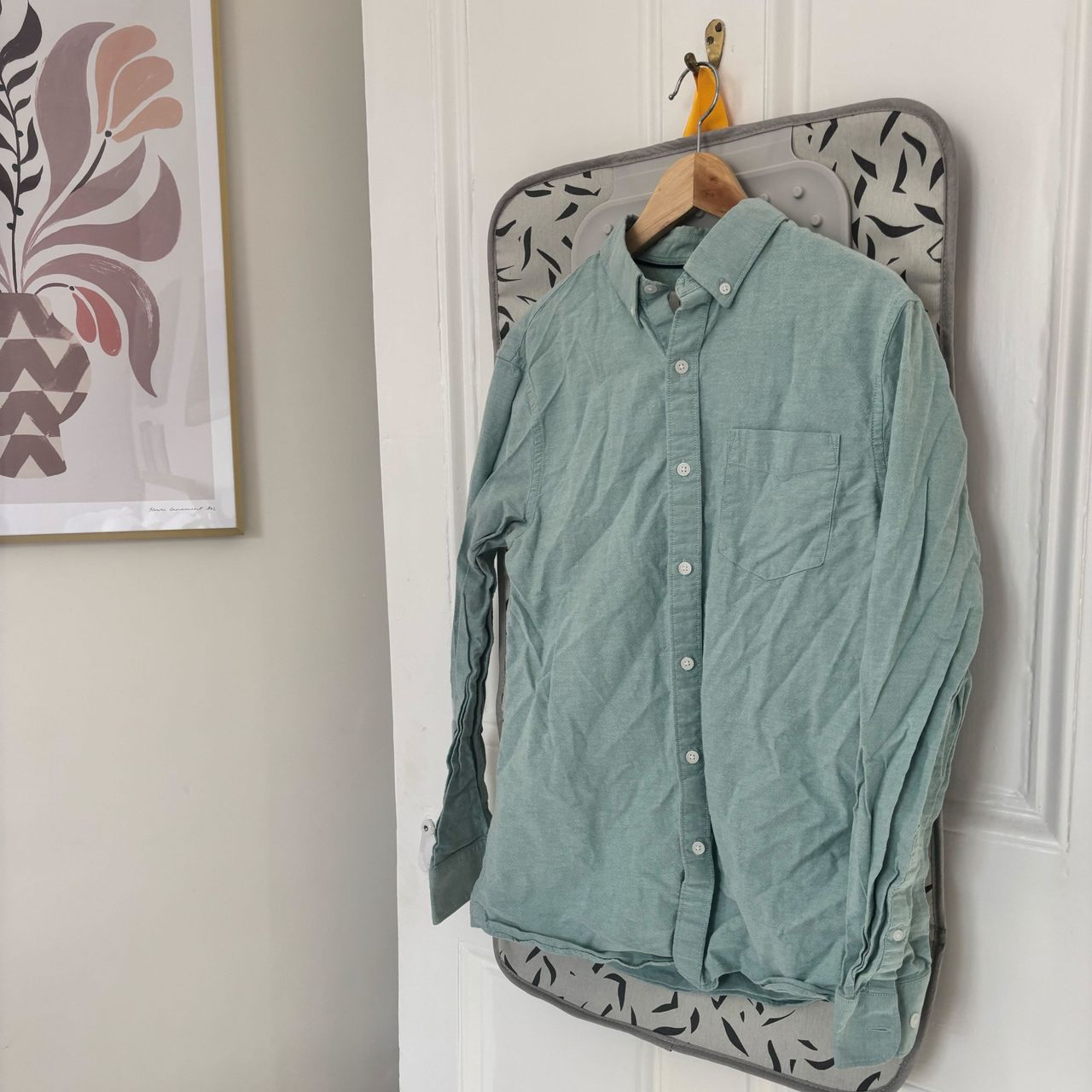 wrinkled green shirt hanging on a door with artwork on wall